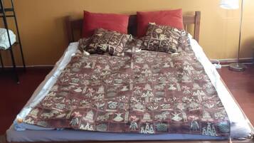 A bed with a patterned bedspread, two red pillows, and a wooden headboard.
