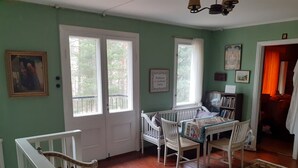 A room with a wooden floor, a white staircase, a crib, a bookshelf, and a window with a view of trees. - Peaceful Pernaja (Loviisa)