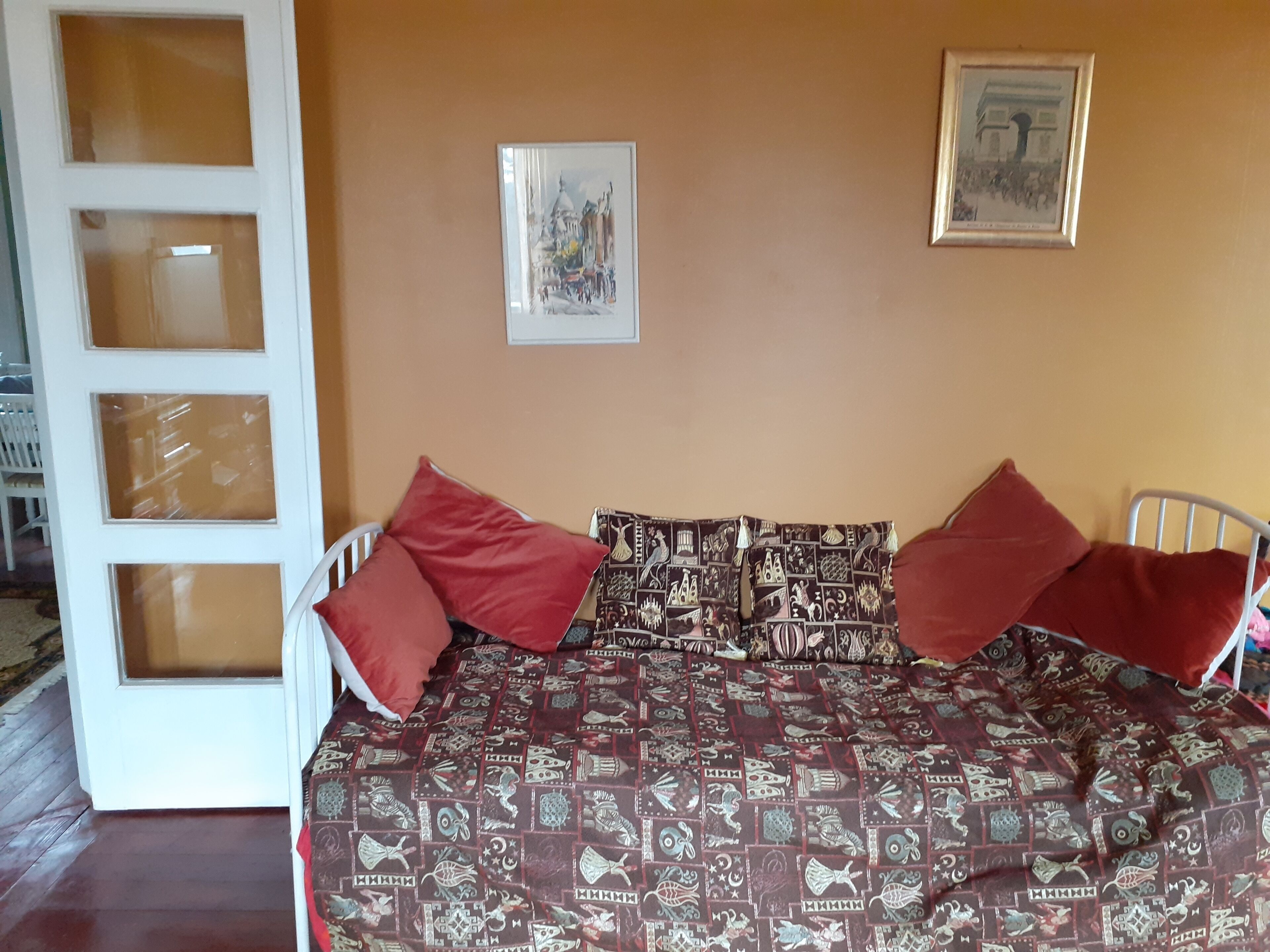 Quarto com uma cama, duas almofadas vermelhas, um cobreleiro estampado e duas imagens emolduradas na parede.