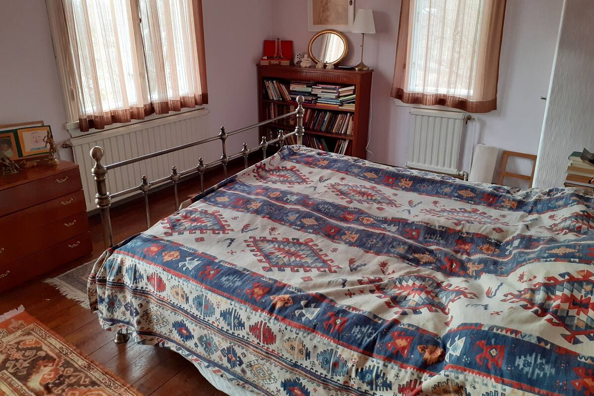 Quarto com cama, cômoda, estante e janela com cortinas.