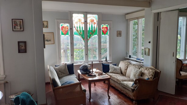 A living room with a sofa, a coffee table, and a wicker chair. There are two windows with stained glass, and a door to the right. - Peaceful Pernaja (Loviisa)