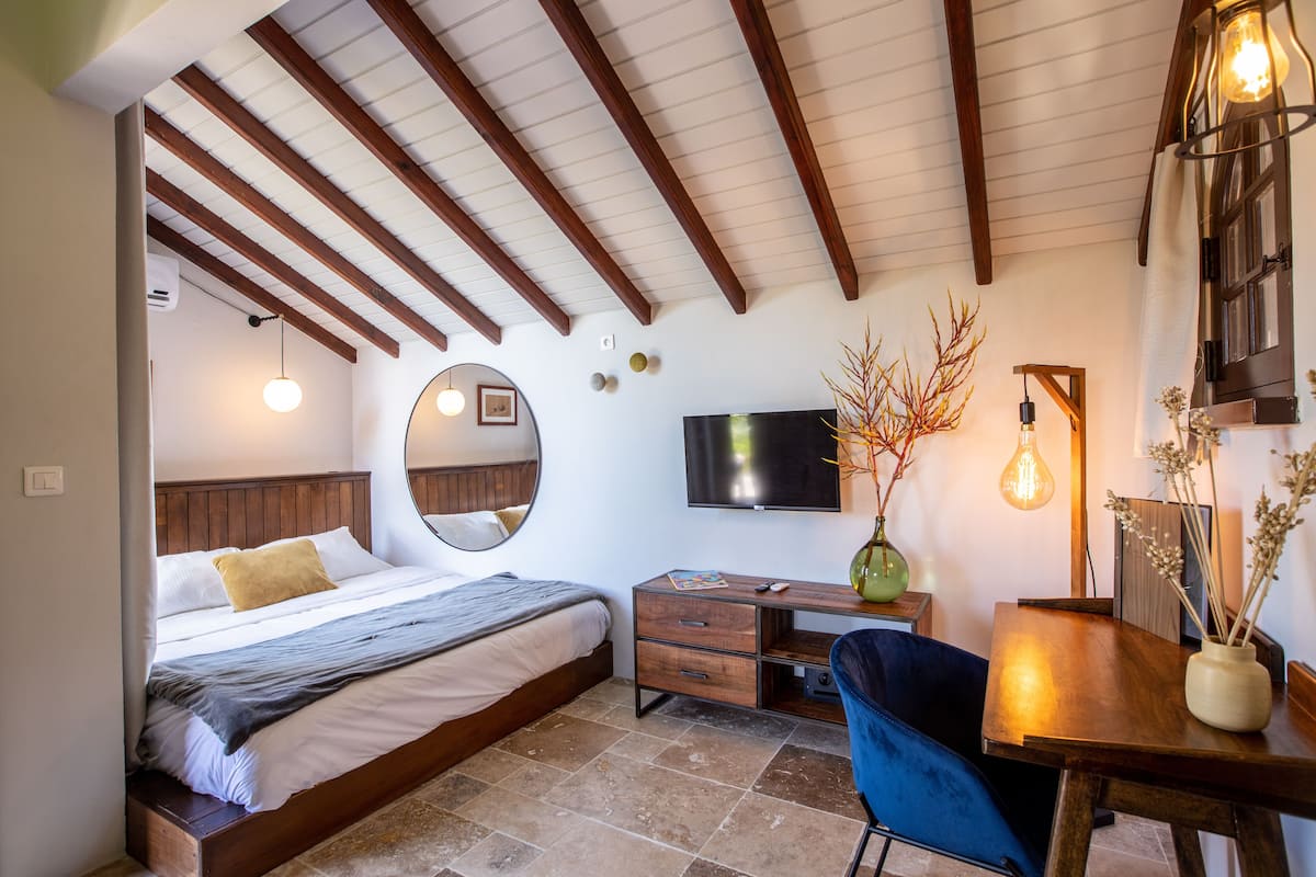 A bedroom with a bed, a desk, a chair, a TV, and a vase with branches.