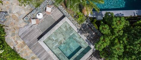 Vista aérea de una zona de piscina con terraza de madera, baldosas de piedra y un pequeño espacio de descanso con sillas y una mesa.