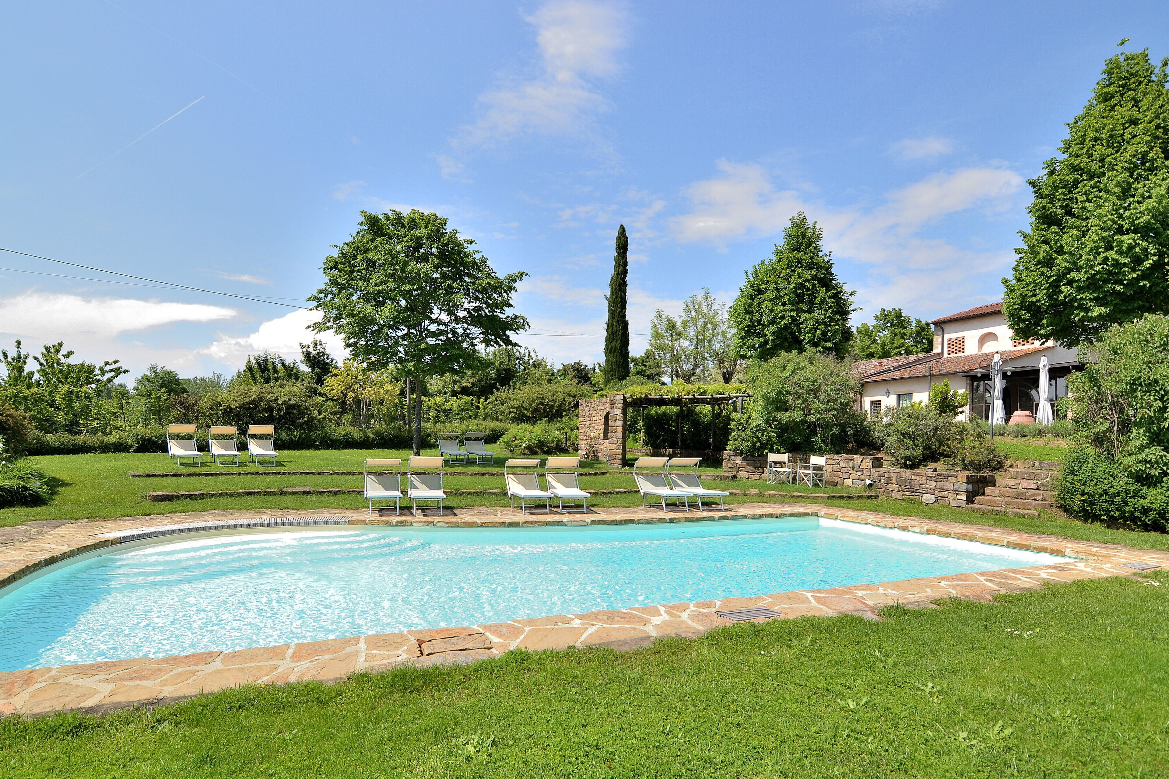 Une piscine entourée de chaises longues, de verdure et d’un mur en pierre.
