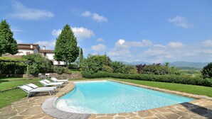 Une piscine aux carreaux de pierre, entourée d’une terrasse en bois et de chaises longues blanches.