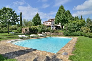 Una piscina rectangular con baldosas de piedra, rodeada por un solárium de piedra. Hay sillas reclinables blancas a lo largo del borde de la piscina.