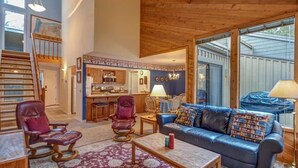 A spacious living room with a large window, a fireplace, and a kitchen area visible through an open door. - Near Marina, stables, great location sleeps 8 (Sunriver)