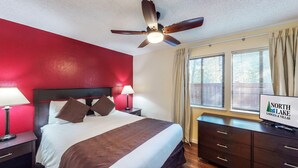 Une chambre d’hôtel comprenant un lit, deux lampes de chevet, un ventilateur de plafond, une table de chevet, une commode et une fenêtre avec des stores.