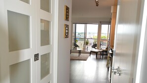 En gang med trægulv, hvide døre med sandblæst glas og udsigt til en balkon med udendørs møbler.