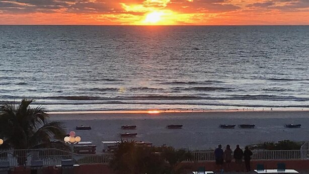 Un atardecer sobre el océano con barcos en el agua y gente en la playa.