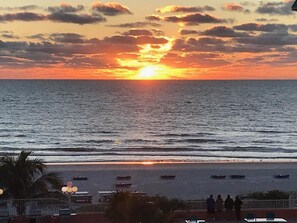 Ein Sonnenuntergang über dem Meer mit Booten auf dem Wasser und Menschen am Strand.