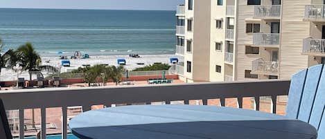 A balcony with a view of the beach and ocean, a pool area, and a building with multiple balconies.