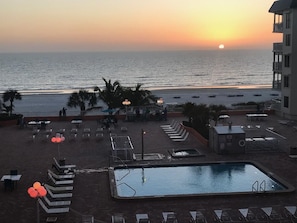 A rooftop pool area with lounge chairs, a small pool, and a view of the sunset over the ocean. - BEACHFRONT BLISS! Beach Cottage #2403 (Indian Shores)