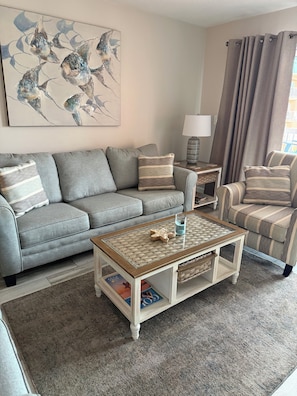 A living room with a grey sofa, striped armchairs, a coffee table, a lamp, and a painting on the wall. - BEACHFRONT BLISS! Beach Cottage #2403 (Indian Shores)