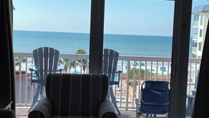 Un balcón con dos sillones a rayas y una silla plegable azul, con vista a una playa con palmeras y una vista despejada del océano.