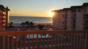 Un hotel frente a la playa con piscina, tumbonas y vista al océano al atardecer.