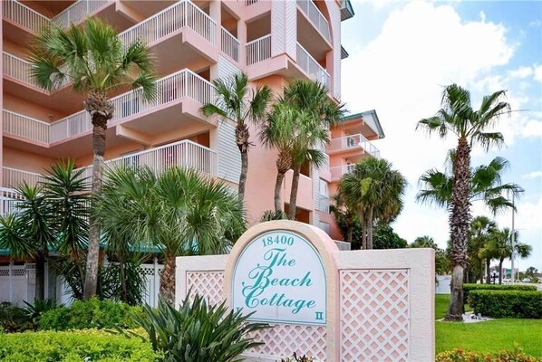 A multi-story building with balconies, palm trees, and a sign reading "The Beach Cottage."