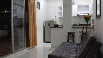 Una sala de estar moderna con un sofá, un ventilador de techo y una cocina al fondo.