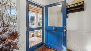Eine blaue Tür mit Glasscheibe, eine weiße Wand mit Ablage und ein Holzdeck, der durch die Tür sichtbar ist.