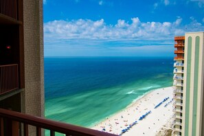 A high-rise hotel with a beach view, featuring balconies with ocean views, a sandy beach with umbrellas, and clear blue skies. - 2128 Pool & Beach views,  w/ two parking passes, spectacular lagoon-style pool (Panama City Beach)