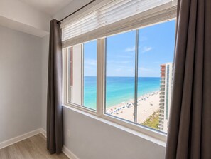 A room with a large window overlooking a beach and a building.