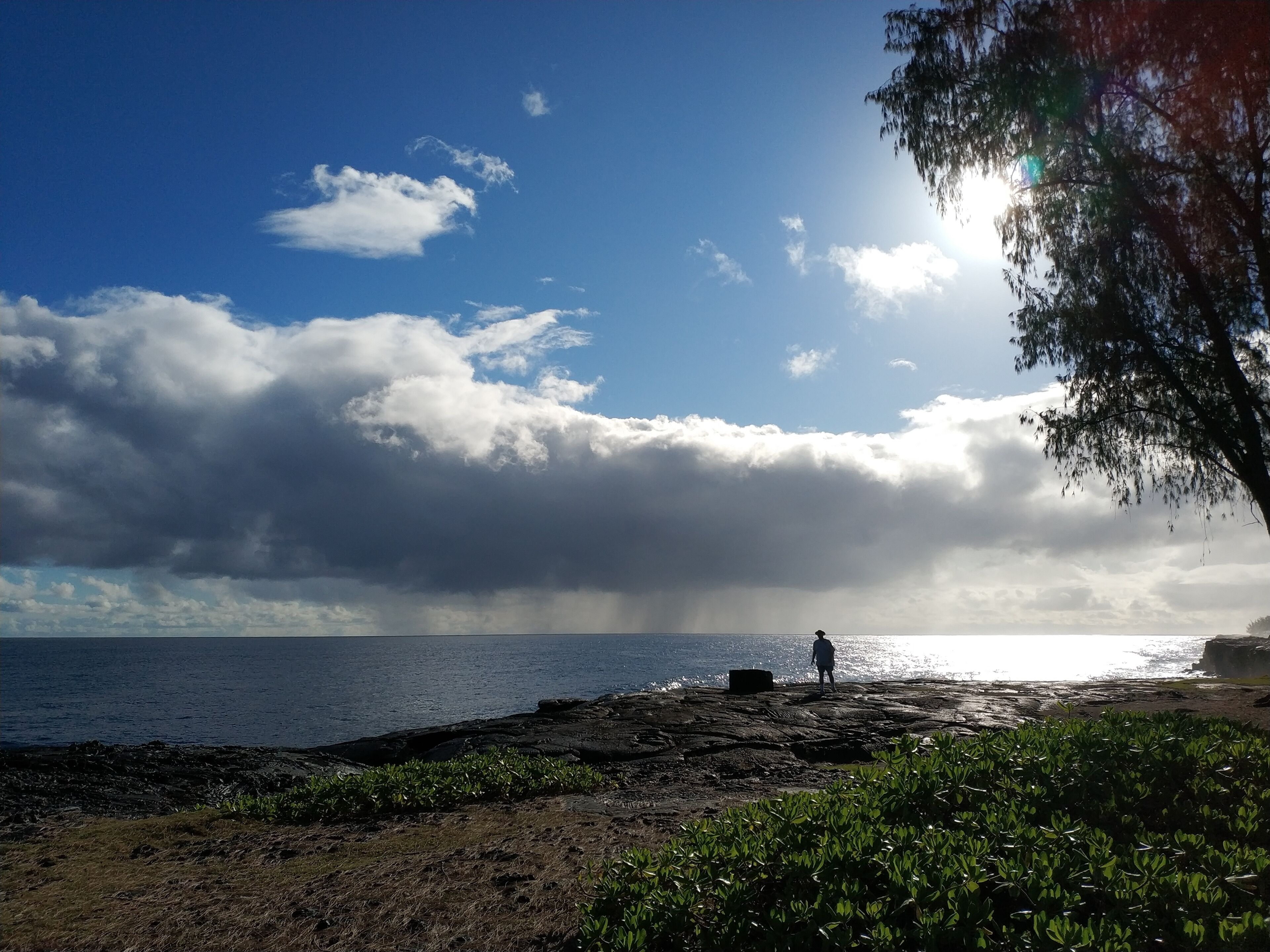 Costa rocosa con una persona de pie, contemplando el mar bajo un cielo parcialmente nublado.