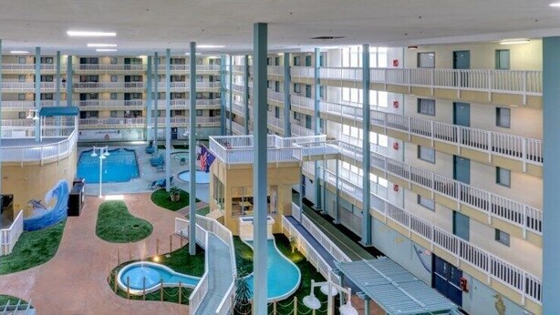 Een hotelatrium met meerdere niveaus, een centraal zwembad, diverse balkons en een speelruimte voor kinderen.