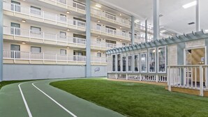 Een meerhoog gebouw met een groene kunstgrasbaan, witte leuningen en een glazen uitbouw met uitzicht op het interieur.