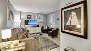 Een moderne woonkamer met een bank, salontafel en televisie. Op de muren staan decoratieve items en er hangt een lijst met een afbeelding van een zeilboot.