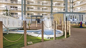 Een meerhoog hotel met balkons, een klein zwembad en een kinderspeelplaats.