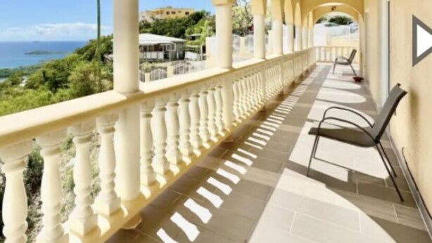 Een overdekt balkon met uitzicht op zee, voorzien van een betegelde vloer en witte balustrades.