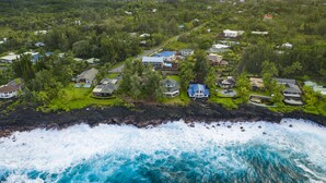 Vue aérienne d’une zone résidentielle côtière, avec des maisons, une côte rocheuse et l’océan.