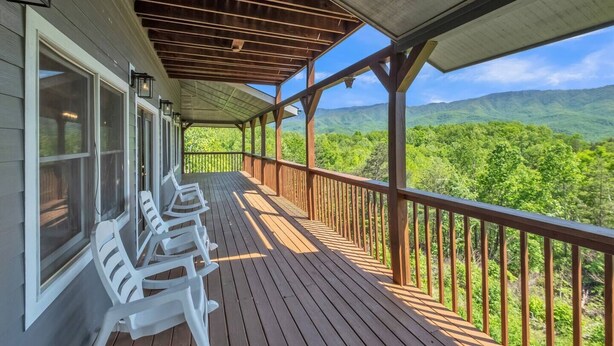 A covered porch with wooden railings and white plastic chairs, overlooking a mountainous landscape.