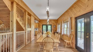 A spacious wooden dining area with a long table and chairs, a staircase on the left, and a door leading outside.