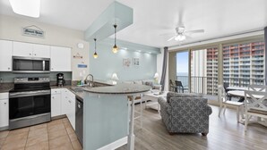 Una cocina moderna con una isla central, un comedor con vistas al balcón y una sala de estar con sofá y sillones.