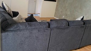 Una sala de estar moderna con un amplio sofá seccional gris, un televisor de pantalla plana montado en la pared y un cuadro abstracto de gran tamaño en la pared.