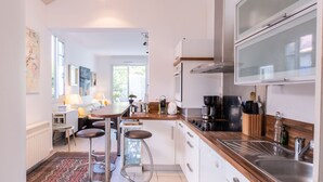 Moderni keittiö, jossa on keskeinen keittiösaareke, baarituolit, ruokailutila ja suuri ikkuna.