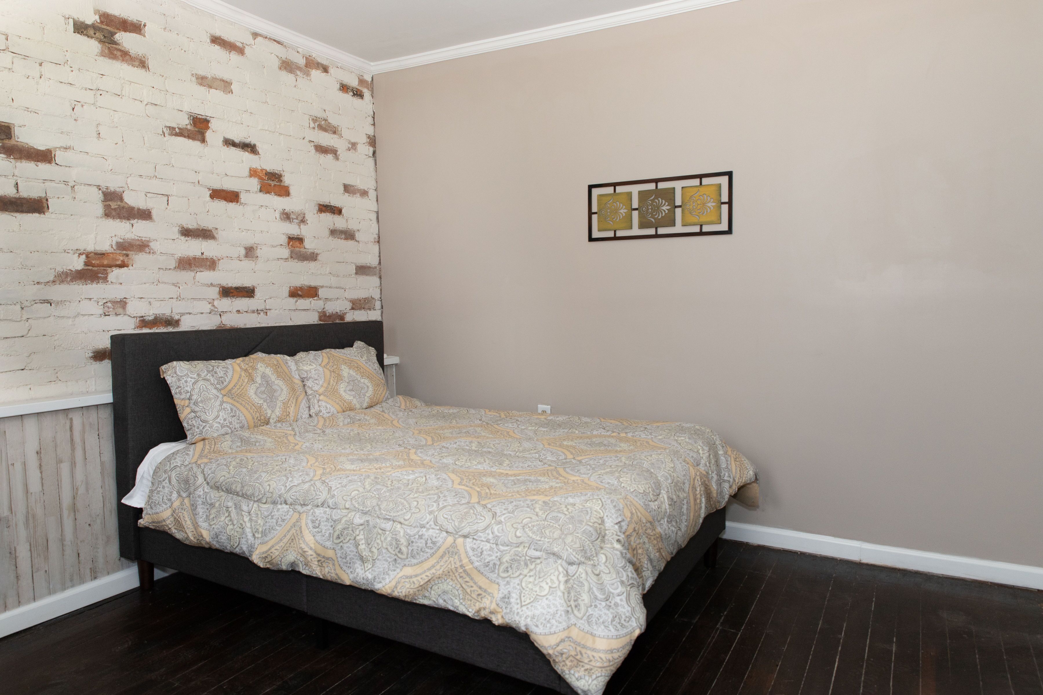 A bedroom with a bed, a brick wall, and a wall-mounted artwork.
