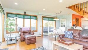 A spacious living room with a brown leather sofa, a wooden coffee table, and a dining area with white chairs. - Cozy Beach House with 270° Spectacular Views (Fairhaven)