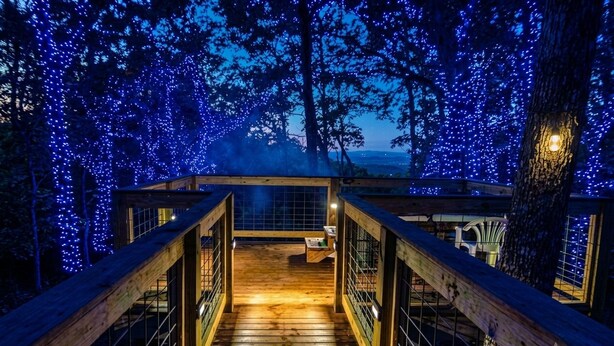 A wooden deck with railings leading to a covered area, surrounded by trees adorned with blue lights. - ROD RUN! Breathtaking View,Hot Tub, Pet Friendly,9.8🌟 Rated










 (Sevierville)