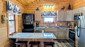 Une cuisine chaleureuse, aménagée dans le style d’un chalet, avec des murs en bois, un îlot central et les équipements de base, notamment un réfrigérateur, une cuisinière et un évier.