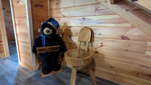 A wooden chair with a 'WELCOME' sign, a plush teddy bear, and a wooden staircase.