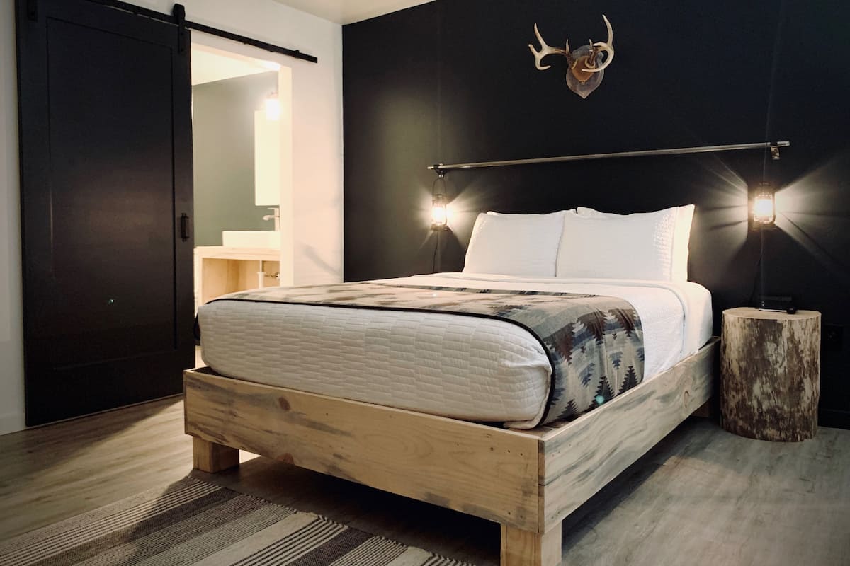 A bedroom with a wooden bed, a black wall with a mounted deer head, and two bedside lamps.