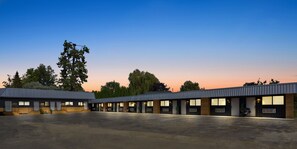 A motel with multiple rooms, a covered parking area, and a large tree in the background.