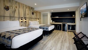 Habitación de hotel con dos camas, una pared de acento de madera, una pequeña cocina americana y un televisor de pared.
