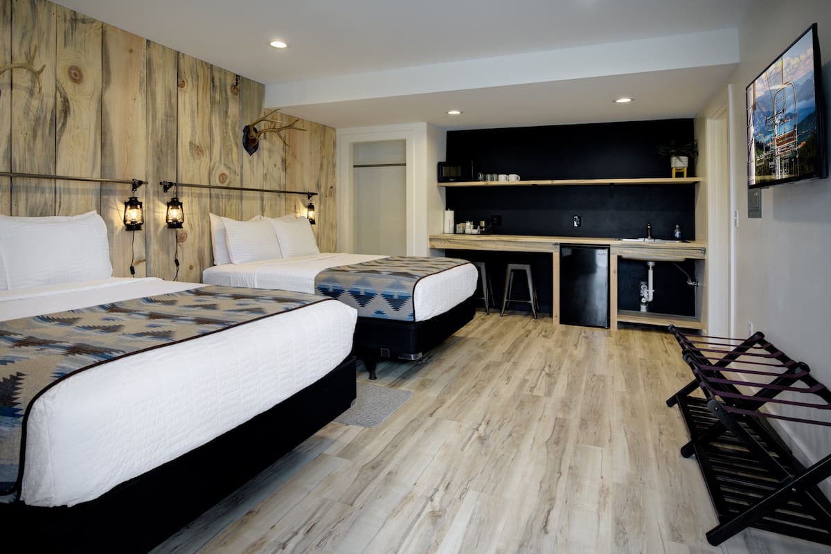 A hotel room with two beds, a wooden accent wall, a small kitchenette, and a mounted TV.