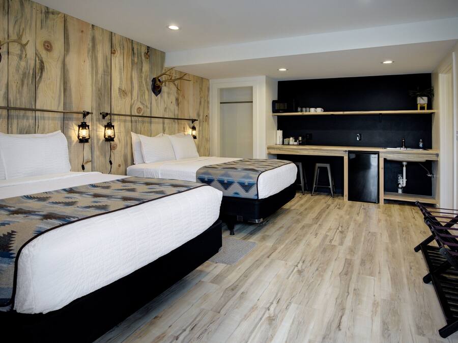 Habitación de hotel con dos camas, una pared de acento de madera, una pequeña cocina americana y un televisor de pared.