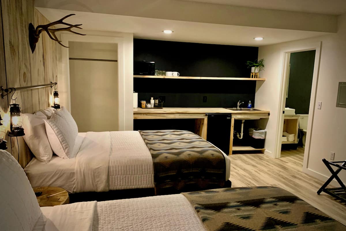 A compact hotel room with a bed, bedside table, and a small kitchenette.