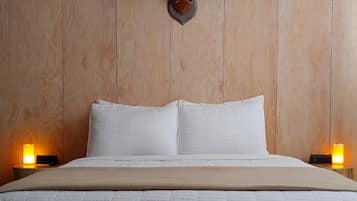 Un lit avec une literie blanche, deux lampes de chevet et une tête de cerf fixée au mur.