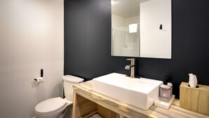 Un baño moderno con un lavamanos blanco, paredes oscuras y un espejo grande.